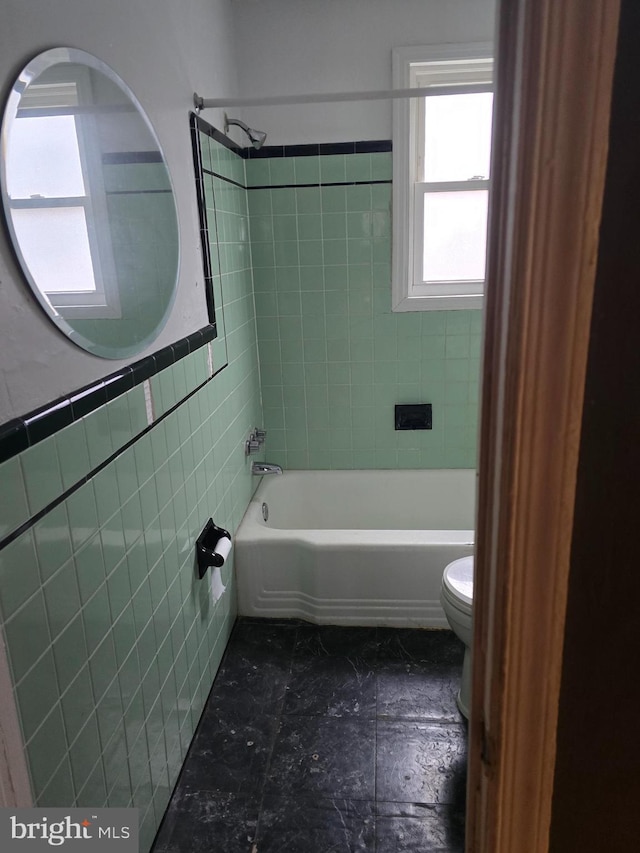 bathroom featuring tile walls, tiled shower / bath combo, and toilet