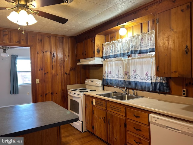 kitchen with sink, white appliances, ceiling fan, wood-type flooring, and wood walls