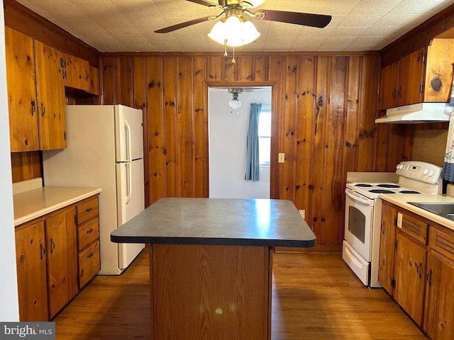 kitchen featuring a kitchen island, wood walls, ceiling fan, dark wood-type flooring, and white appliances