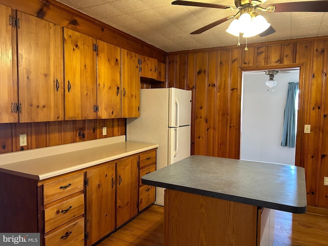 kitchen featuring ceiling fan, hardwood / wood-style floors, white fridge, and wood walls