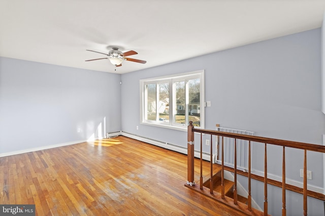 empty room featuring ceiling fan, light wood-type flooring, and a baseboard heating unit