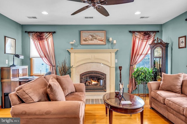 living room featuring ceiling fan, a fireplace, and light hardwood / wood-style floors