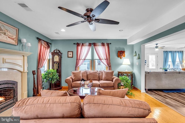 living room featuring a high end fireplace, ceiling fan, and light wood-type flooring