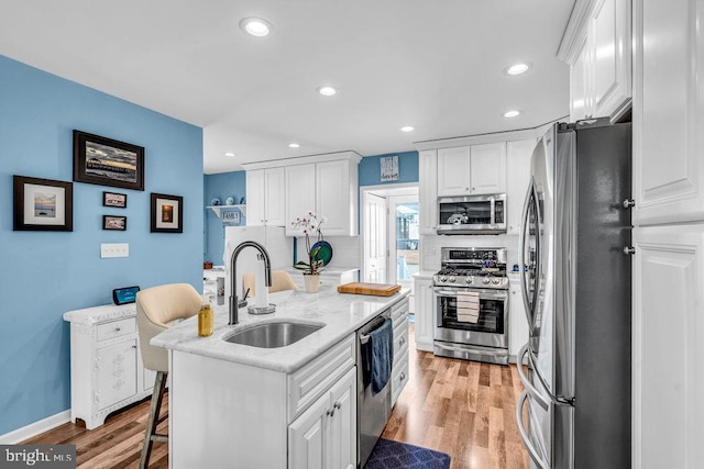 kitchen with white cabinetry, sink, stainless steel appliances, and a center island with sink