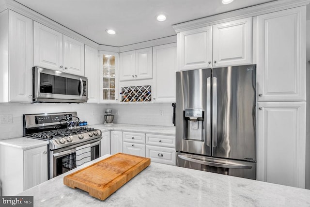 kitchen featuring stainless steel appliances, white cabinetry, light stone countertops, and backsplash