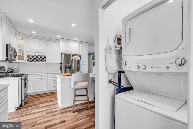 laundry area with stacked washer / drying machine and light wood-type flooring