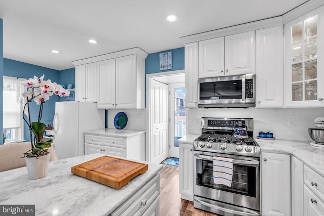 kitchen with tasteful backsplash, light hardwood / wood-style flooring, stainless steel appliances, light stone countertops, and white cabinets