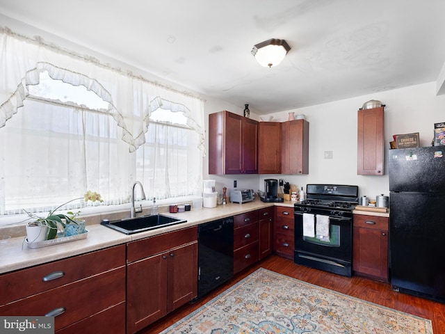 kitchen featuring dark wood-style flooring, light countertops, a sink, dark brown cabinets, and black appliances