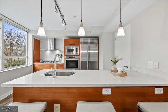 kitchen with built in appliances, wall chimney range hood, a breakfast bar area, and sink