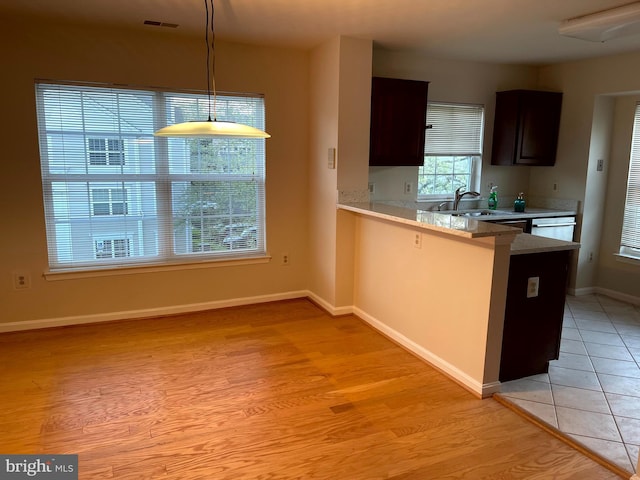 kitchen featuring sink, dark brown cabinets, light hardwood / wood-style floors, decorative light fixtures, and kitchen peninsula