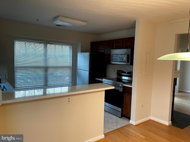 kitchen with stainless steel appliances, light stone countertops, dark brown cabinets, and light wood-type flooring