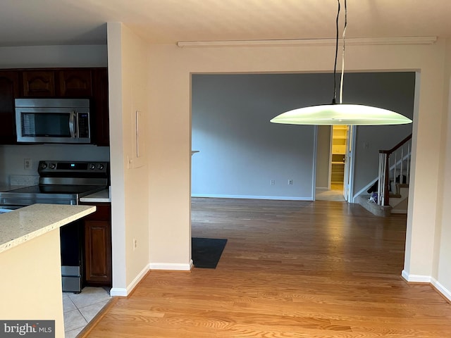 kitchen featuring light hardwood / wood-style flooring, dark brown cabinets, light stone countertops, and appliances with stainless steel finishes