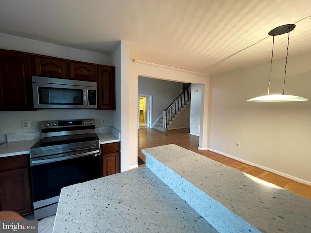 kitchen with light stone counters, wood-type flooring, dark brown cabinets, appliances with stainless steel finishes, and pendant lighting