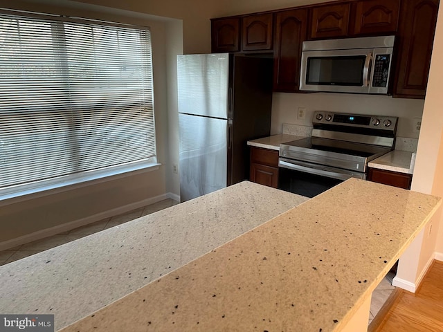 kitchen with dark brown cabinetry, light tile patterned flooring, light stone countertops, and appliances with stainless steel finishes