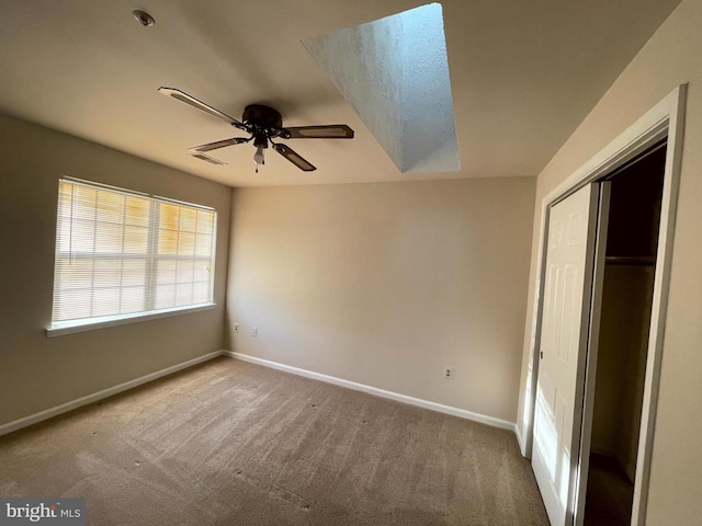 unfurnished bedroom with a skylight, carpet floors, ceiling fan, and a closet