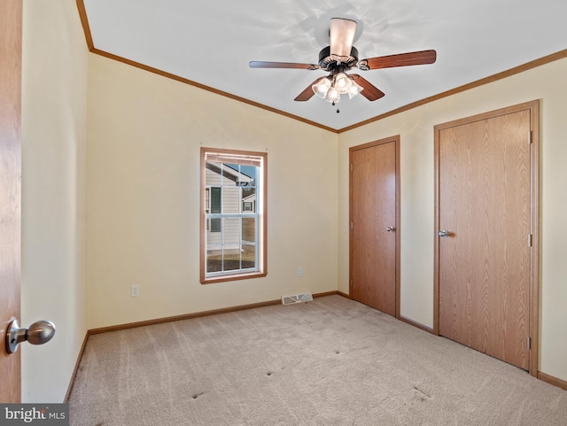 unfurnished bedroom with two closets, ornamental molding, light colored carpet, and ceiling fan