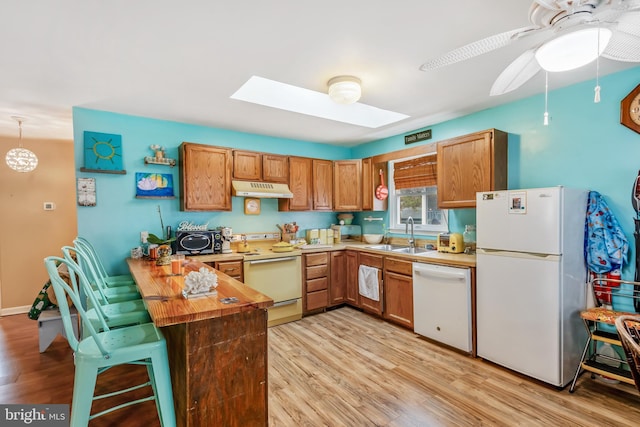 kitchen featuring white appliances, a skylight, butcher block counters, under cabinet range hood, and a sink