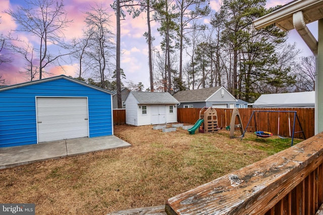 view of yard featuring an outbuilding, a playground, a storage unit, concrete driveway, and a fenced backyard