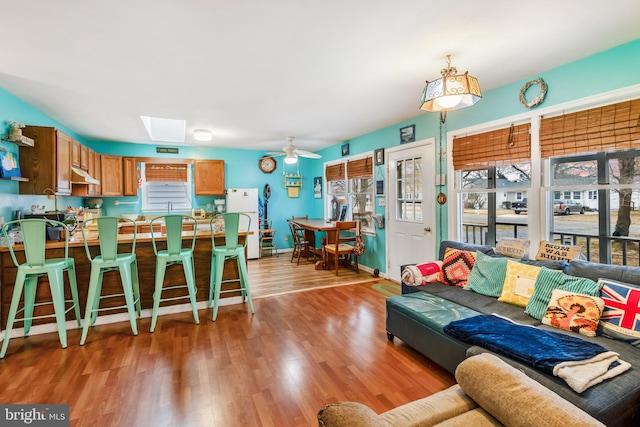 living area featuring light wood-type flooring, a skylight, baseboards, and a ceiling fan