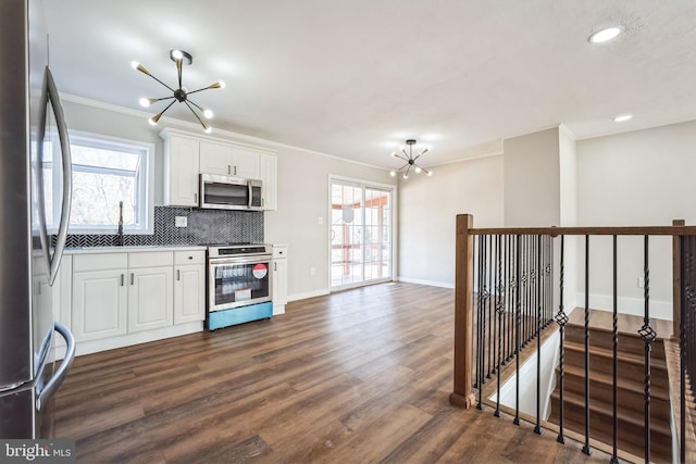 kitchen featuring appliances with stainless steel finishes, a healthy amount of sunlight, white cabinets, decorative backsplash, and a chandelier