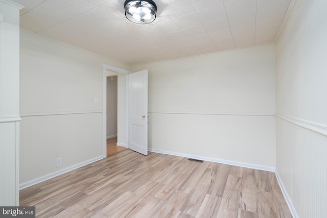 empty room with crown molding and light wood-type flooring