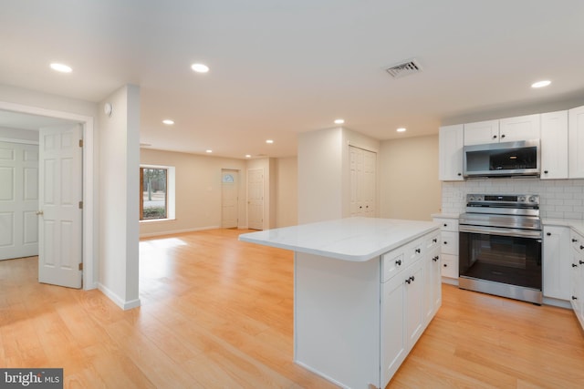 kitchen with stainless steel appliances, a center island, white cabinets, and light wood-type flooring