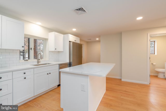 kitchen with a kitchen island, appliances with stainless steel finishes, white cabinetry, sink, and light wood-type flooring