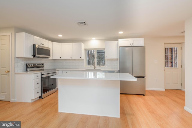 kitchen featuring sink, appliances with stainless steel finishes, white cabinetry, a center island, and light hardwood / wood-style floors