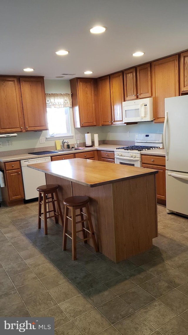 kitchen featuring white appliances, a breakfast bar, a center island, and sink