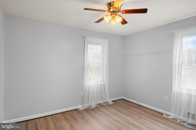 empty room with healthy amount of natural light, wood finished floors, ceiling fan, and baseboards
