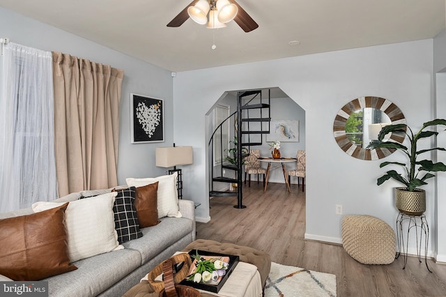 living area featuring baseboards, ceiling fan, wood finished floors, and stairs