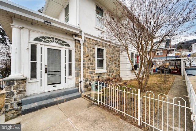 view of exterior entry featuring stone siding and fence