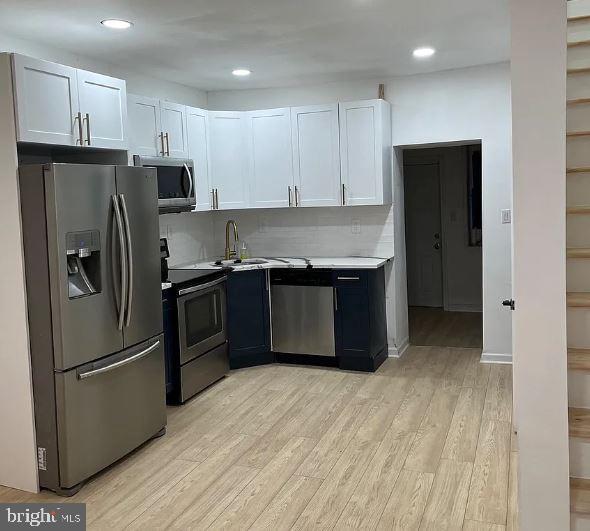 kitchen featuring appliances with stainless steel finishes, light hardwood / wood-style floors, decorative backsplash, and white cabinets