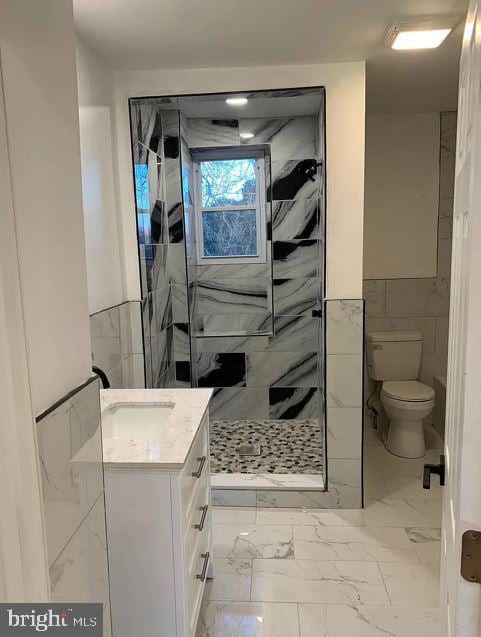 bathroom with vanity, toilet, tile walls, and a tile shower