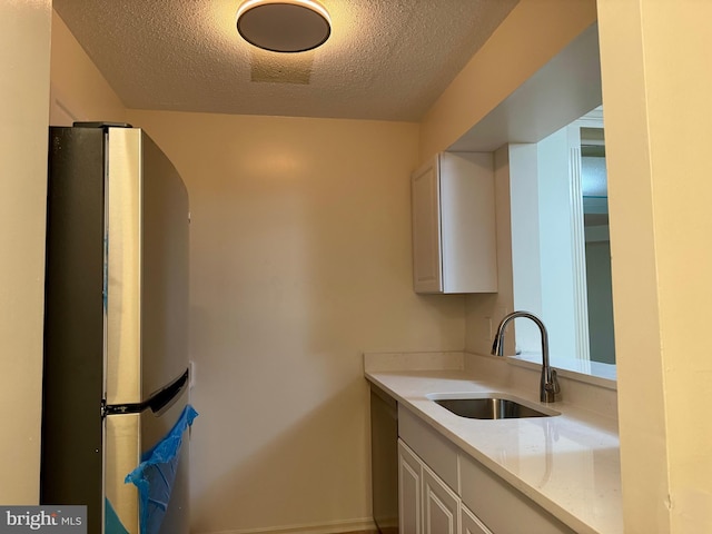 kitchen with a sink, a textured ceiling, white cabinets, and freestanding refrigerator