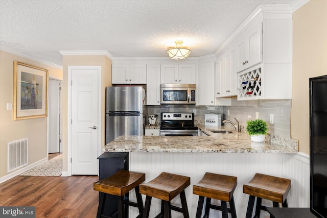 kitchen featuring stainless steel appliances, kitchen peninsula, hardwood / wood-style floors, and white cabinets