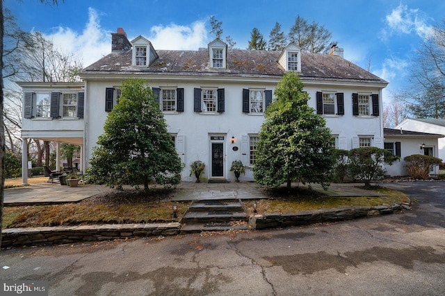 view of front facade featuring a patio, a chimney, a high end roof, and stucco siding