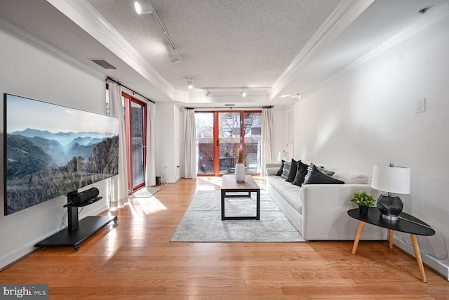 living room with ornamental molding, a raised ceiling, a textured ceiling, and light hardwood / wood-style flooring