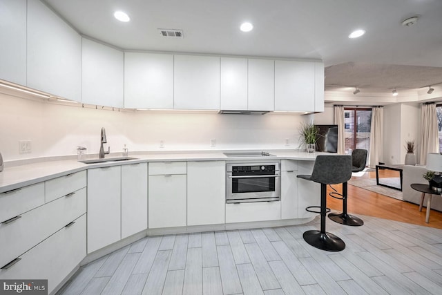 kitchen with black electric cooktop, sink, oven, and white cabinets