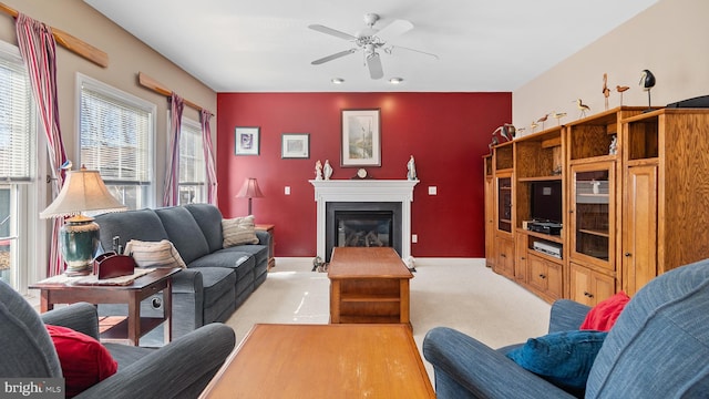 living area with light carpet, ceiling fan, a glass covered fireplace, and baseboards