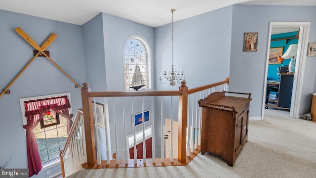 hall featuring a healthy amount of sunlight, a notable chandelier, and an upstairs landing