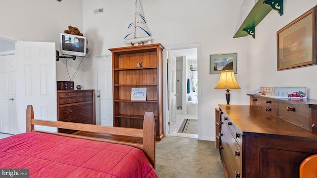 bedroom featuring visible vents, baseboards, light colored carpet, a towering ceiling, and ensuite bath