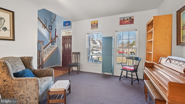 living area featuring stairs, dark carpet, and baseboards