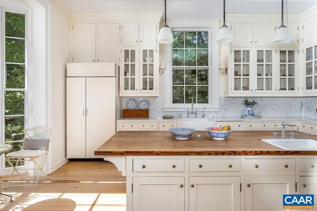 kitchen featuring pendant lighting, butcher block countertops, sink, white cabinets, and decorative backsplash