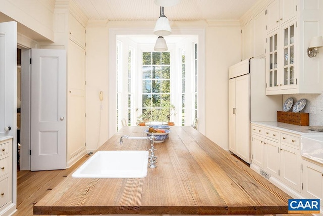 kitchen with pendant lighting, sink, ornamental molding, and white cabinets