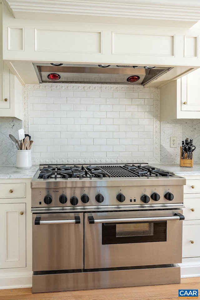 kitchen featuring extractor fan, white cabinetry, double oven range, light stone countertops, and decorative backsplash