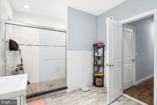 bathroom with hardwood / wood-style flooring, a shower with shower door, and tile walls