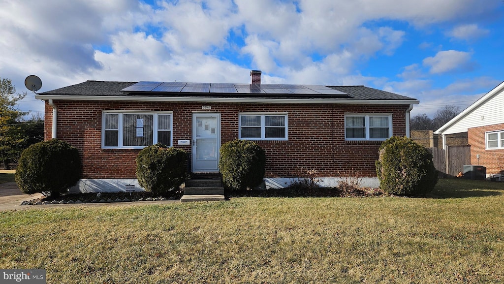 view of front facade with a front yard, central AC unit, and solar panels