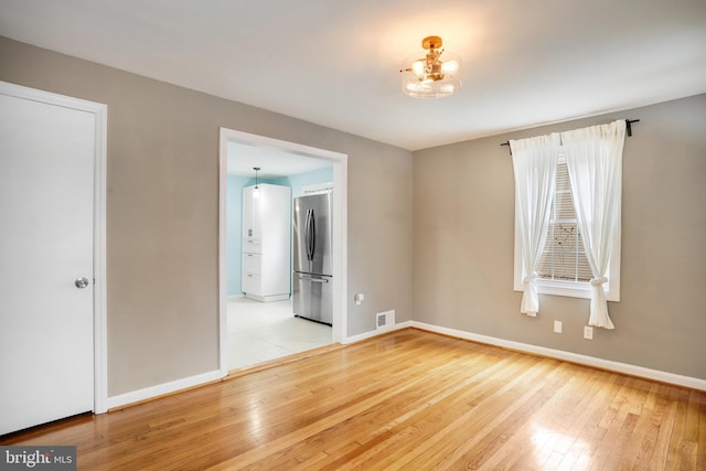 unfurnished room featuring a notable chandelier and light hardwood / wood-style floors