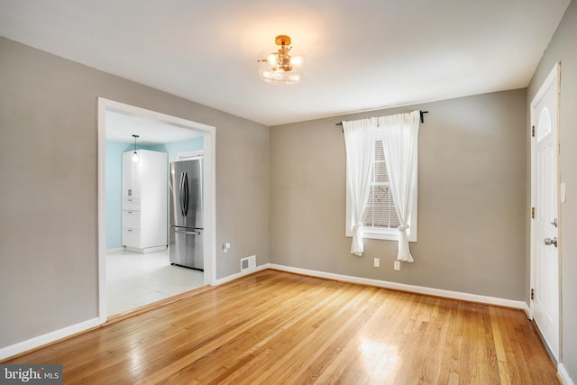 unfurnished room featuring a chandelier and light hardwood / wood-style flooring